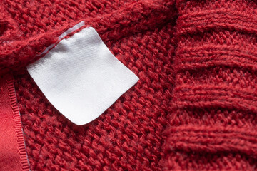 Blank laundry care clothes label on red knitted fabric texture background
