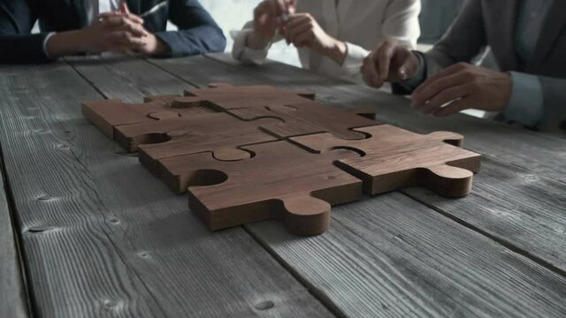 Business people assembling wooden puzzle on work table, teamwork concept