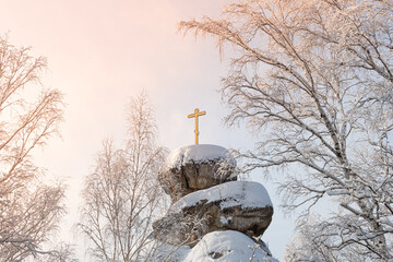 Christian cross on rock in winter forest. Golden cross on stone  with snow.