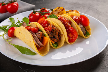 traditional Taco with meat, tomatoes, beans, chili peppers and grilled corn on a white plate and dark background for the restaurant menu