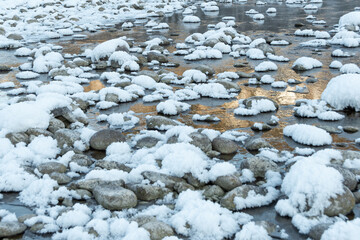 Boulders in cold water are covered with snow. Winter river on frosty morning.