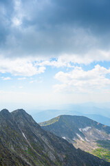 Panoramic view of rocky ridge. Mountains on horizon under cloudy sky. Travel through mountain valley on sunny day.