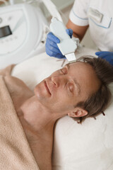 Fototapeta na wymiar Vertical shot of a mature man getting ultrasound skin cleanse by beautician