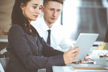 Fototapeta premium Business woman and man discussing questions while using tablet computer at workplace in modern office. Teamwork, meeting and brainstorming concept