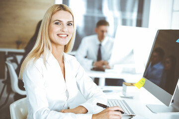 Fototapeta premium Business woman using computer at workplace in modern office. Secretary or female lawyer smiling and looks happy. Working for pleasure and success