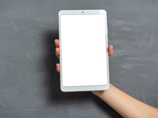 a woman's hand holds a white tablet on a gray textured background. Place to insert on the screen of...