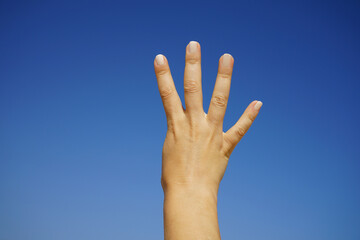 women's hands show the number four against a cloudless blue sky