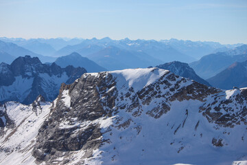 Fototapeta na wymiar Top of Germany: A large view to the snow coverered and rocky mountain ranges of the Alps from the glacier of the highest german mountain Zugspitze on a beautiful sunny day 