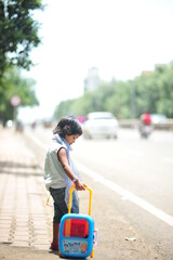 a kid with toy luggage waiting for transport on the side of the road