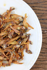 Fried giant catfish and pile of Deep fried small fishes (Minnow fish) Traditional Thai recipes in white dish on rustic wood background.  popular in Thailand, important export product of Thailand.