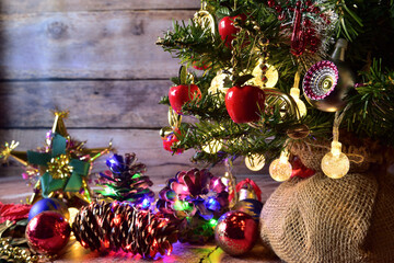 Christmas tree, background on wooden boards. Decorations of multicolored illuminated pinecones, bell, apples, garlands of warm lights. Red, blue, green, gold colors. Place to write.