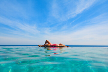 Happy girl have fun on summer beach holiday. Young woman relaxing at edge of infinity swimming pool...