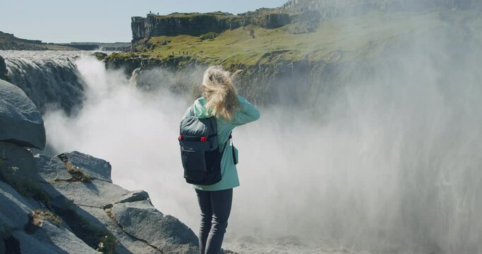 Woman standing at cliff edge looking at Detifoss waterfall in Iceland