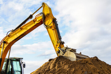 a yellow excavator boom with a bucket digs a pile of earth