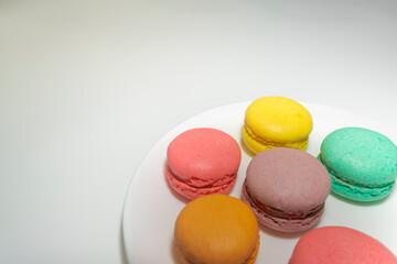 multicolored macaroons on a white plate on a gray background