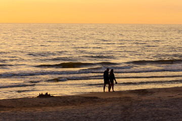 People walking by the sand beach at sunset