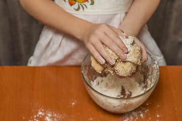 A girl in a kitchen apron is kneading cookie dough. Homemade baking.