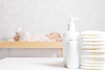 Fototapeta na wymiar Infant baby care products. Lotion, powder and diapers on changing table in nursery. Baby cosmetics and hygiene concept.