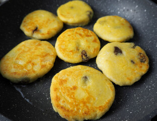 seven yellow curd cheesecakes without sugar with a banana in corn flour fried in coconut oil in a gray frying pan side view . cooking cheesecakes at home