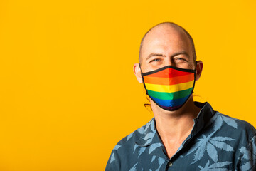 Portrait of a young adult man wearing a facial mask with the colors of the rainbow, against a yellow background
