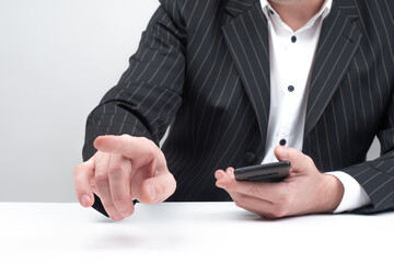 Businessman with a telephone. Human in a business suit holds a smartphone. Man with a smartphone shows a finger. Businessman makes a hand gesture. Businessman sits at a desk. Business negotiations
