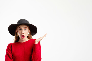 Omg face. Best trends. Personal offer. Fashion look. Information banner. Shocked woman in red sweater black hat pointing copy space isolated on white.