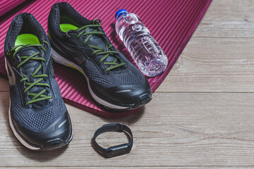 sport equipment with sport shoes, pilates mat, smart watch and bottle of water on a wooden floor