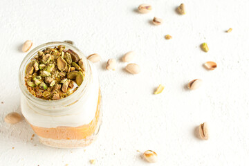 Pistachios in Glass Mason Jar Mugs with pumpkin parfait on a white plate, pistachios scattered on the table.