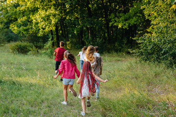 A group of happy children run and play in the Park during sunset. Summer children's camp