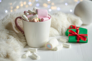 Cup with marshmallows and a gift on a white table.
