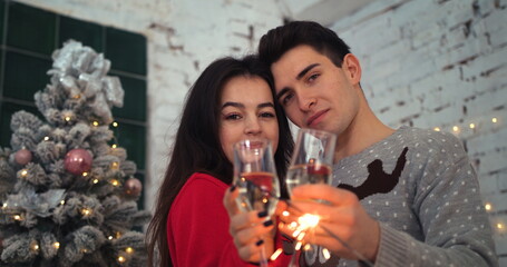 Girl and boyfriend kissing while holding sparklers and glasses of champagne then looking at camera. Christmas atmosphere