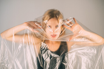 Naklejka premium Stop violence. Defocused art portrait. Female rights. Woman protection. Annoyed disturbed woman trapped in transparent polyethylene film isolated on gray background out of focus.