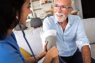 Female nurse measures blood pressure to senior man while being in a home visit.