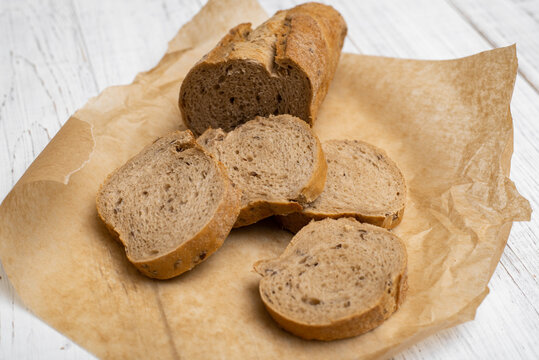 Sliced black mustard bread. Pieces of bread on paper on a white wooden background.