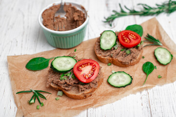 Sandwiches, canapes with chicken pate, tomatoes and cucumbers. On a white wooden background.