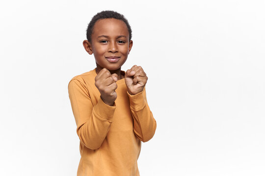 Isolated Shot Of Cute Little African Boy Keeping Fists Clenched Standing In Position To Punch Invisible Enemy, Learning How To Stand Up For Himself, Looking At Camera With Smile, Having Fun