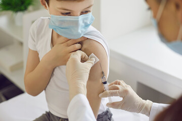 Boy in face mask getting flu shot at doctor's office during World Immunization Week