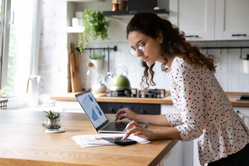Serious young woman wearing glasses calculating finances, household expenses, confident...