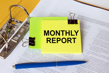 Text Monthly Report on a yellow sticker that is in a folder with documents and a blue pen
