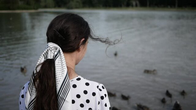 portrait young brunette woman who feeds ducks on lake. summer. view from back