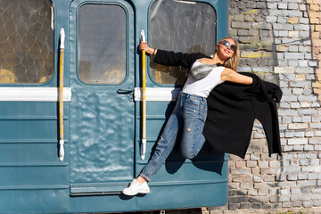 A blonde woman in sunglasses poses on the steps of a museum piece of a train.