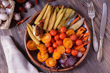 Appetizing grilled vegetables next to spices, fork and knife on a wooden table, top view