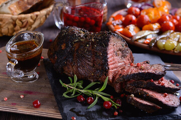 Appetizing roast beef with sauce and spices on a wooden table next to grilled vegetables and cranberry sauce