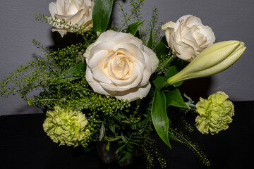A bouquet of funeral flowers. White and yellow flowers with a gray wall background