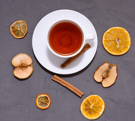 top view of Cup of tea, dried slices of orange and cinnamon with Christmas decorations on a gray wooden background.