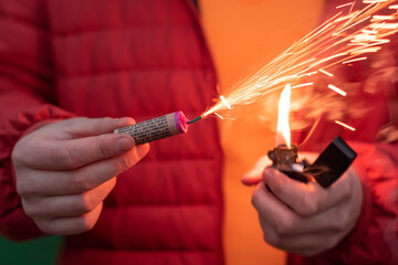 Man in Red Jacked Lighting Up Firecracker in his Hand Using Gasoline Lighter. Guy Getting Ready for...