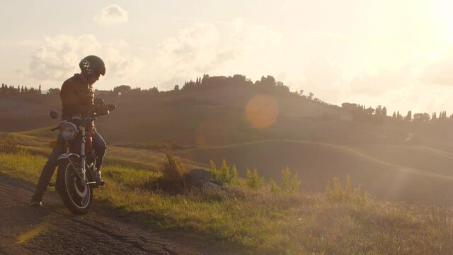 Man on a red motorcycle taking pictures at sunset on road in beautiful hills landscape in Tuscany countryside, Italy. Volterra.
