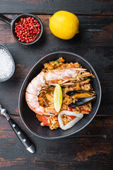 Traditional Spanish paella with seafood and chicken in black bowl  on old dark wooden table, top view