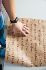 Photo of a youngg and attractive man cutting wrapping paper with scissors to prepare a Christmas present. Top view