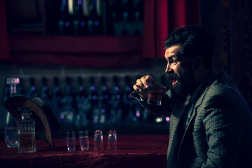 Hipster male with stylish beard drinking cognac, vodka or brandy sitting at the bar. - obrazy, fototapety, plakaty